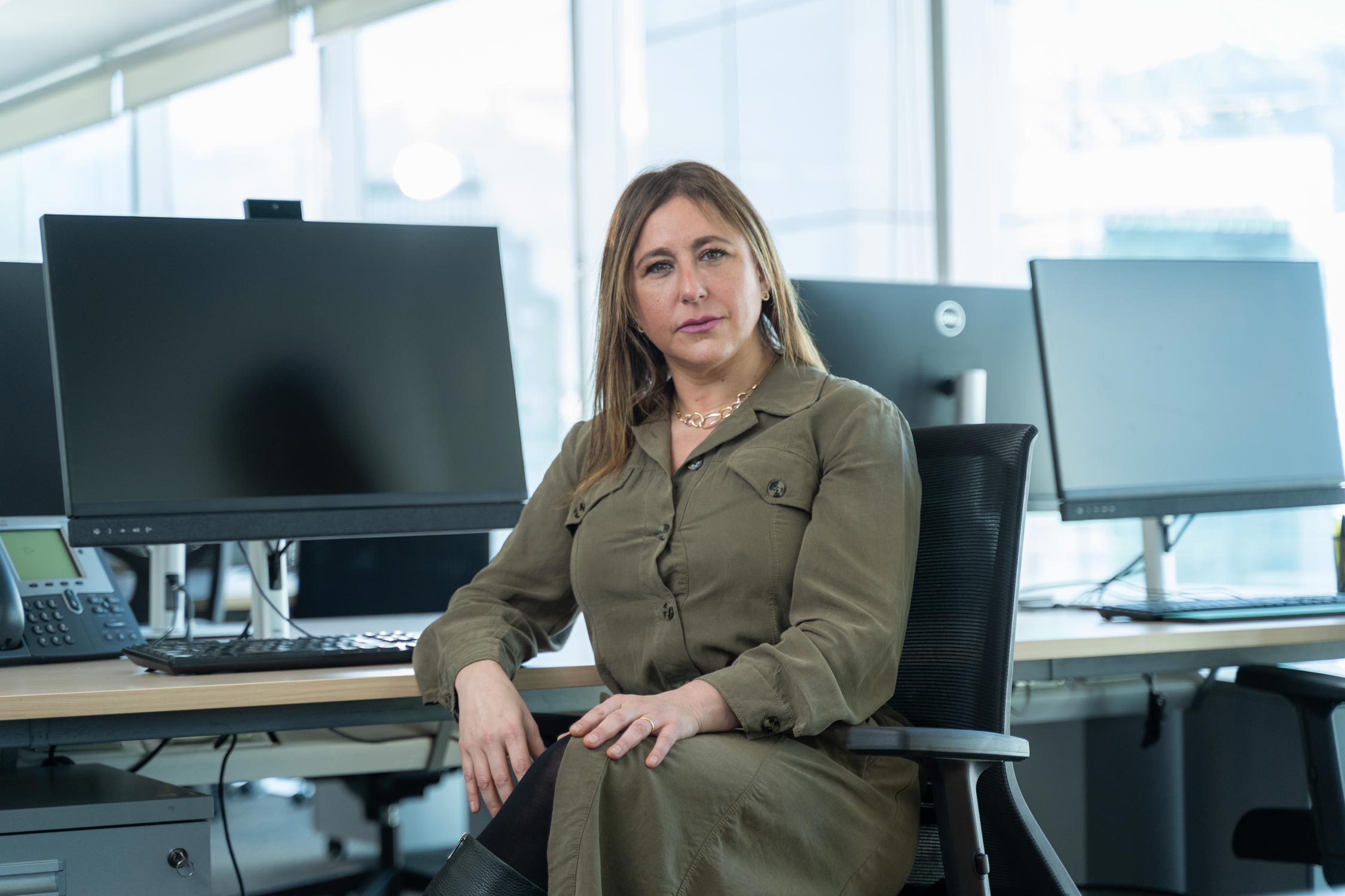 Mujer sentada en una oficina con ordenadores de fondo.