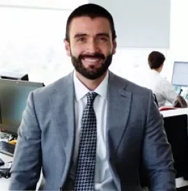 Hombre sonriendo en una oficina con traje gris.