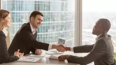 Personas en reunión de negocios estrechando manos en oficina luminosa.