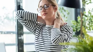 Mujer relajándose en oficina iluminada con plantas alrededor.