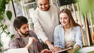 Tres personas trabajando juntas en una oficina moderna con plantas.