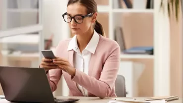 Mujer trabajadora revisando su móvil en una oficina.