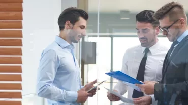 Tres hombres en la oficina revisando documentos.
