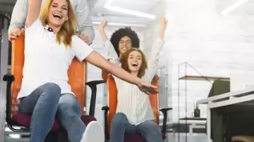 Personas divirtiéndose con sillas de oficina en una oficina moderna.