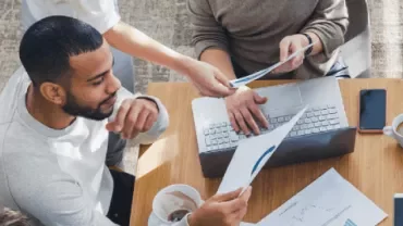 Personas trabajando juntas en una mesa con portátiles y documentos.