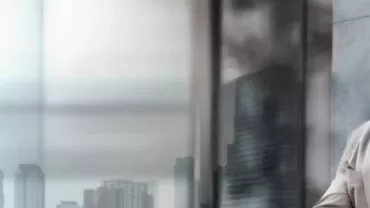 Hombre con mascarilla mirando por la ventana en ciudad moderna.