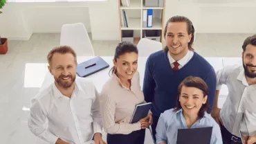 Grupo de personas en una oficina luminosa, sonriendo a la cámara.
