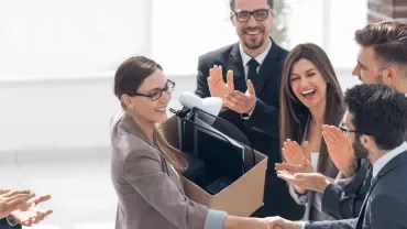 Grupo de personas aplaudiendo a una mujer con caja en oficina.