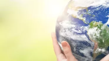 Manos sosteniendo la Tierra sobre un fondo verde borroso.