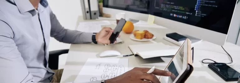 Hombre trabajando en un escritorio con computadora, tablet y móvil.