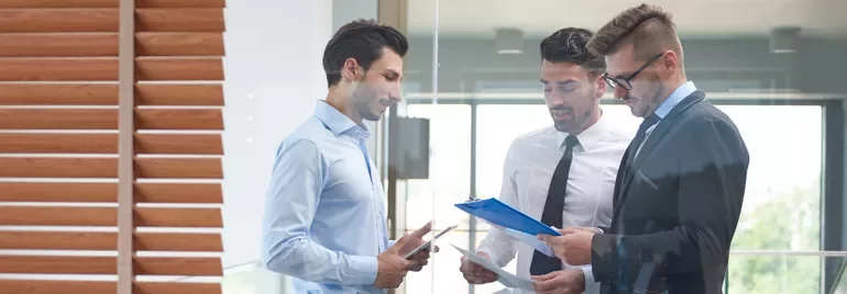 Tres hombres en la oficina revisando documentos.