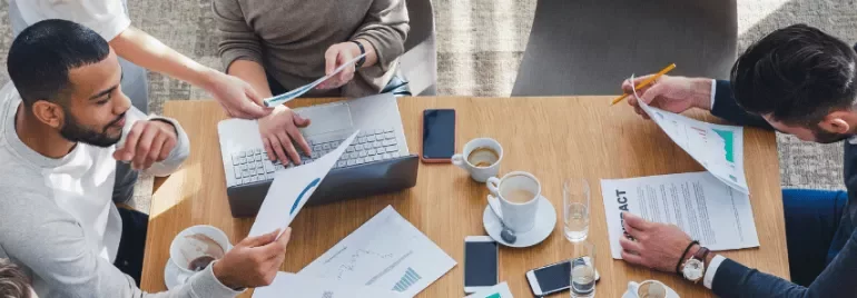 Personas trabajando en equipo con portátiles y documentos en una oficina.