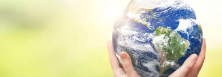 Manos sosteniendo la Tierra sobre un fondo verde borroso.