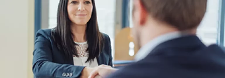 Mujer estrechando la mano a un hombre en una oficina.
