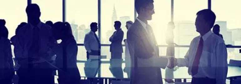 Personas en una reunión de negocios, dos hombres dándose la mano.