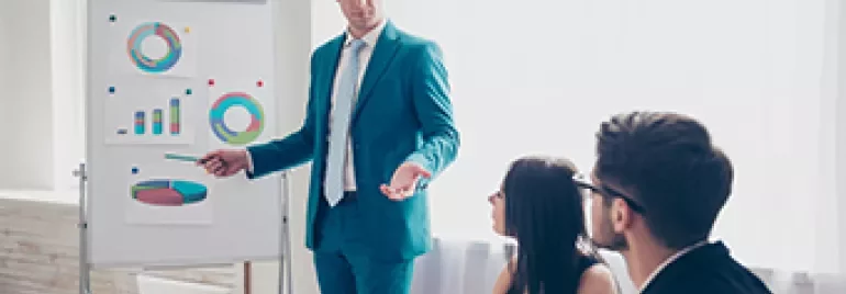 Hombre en traje azul presentando gráficos a colegas en una reunión.