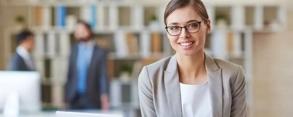 Mujer sonriente con gafas en una oficina moderna.