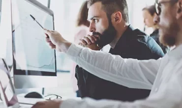 Dos hombres trabajando en una computadora, uno señalando la pantalla.