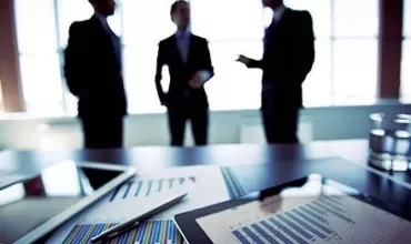 Personas conversando en una oficina con gráficos y tabletas sobre la mesa.