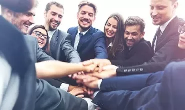 Grupo de personas unidas, sonriendo y colocando las manos juntas.