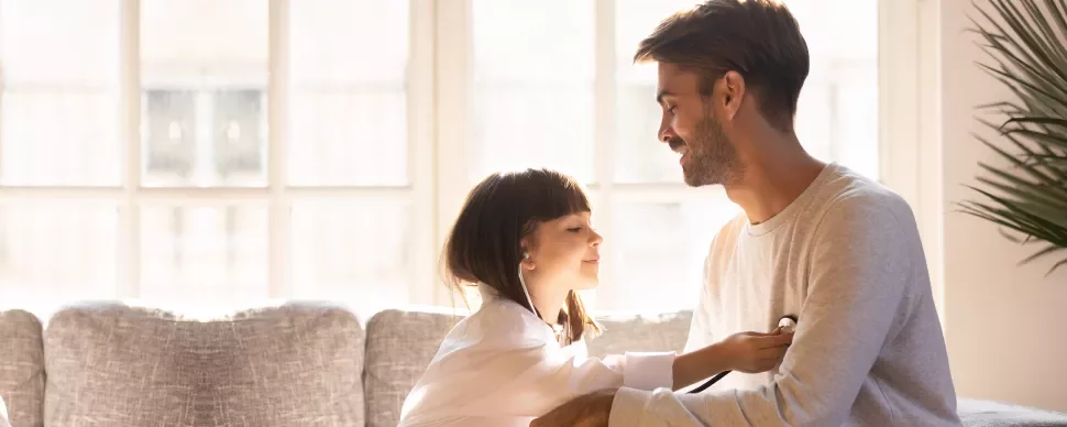 Niña jugando al médico con su padre en la sala.
