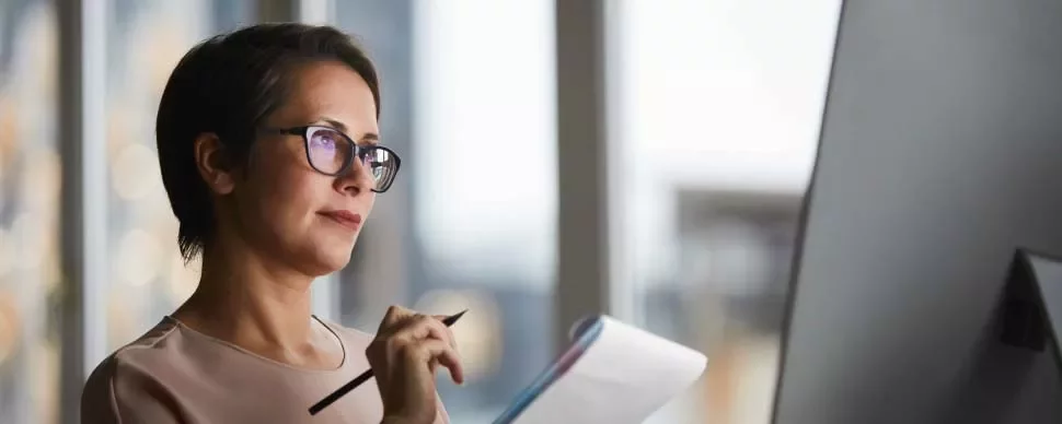 Mujer con gafas y cuaderno frente a una pantalla.