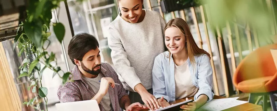 Tres personas trabajando juntas en una oficina moderna con plantas.