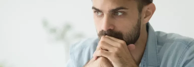 Hombre pensativo con barba y camisa azul claro.