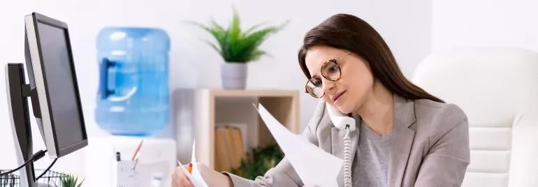 Mujer trabajando en la oficina, habla por teléfono y revisa documentos.