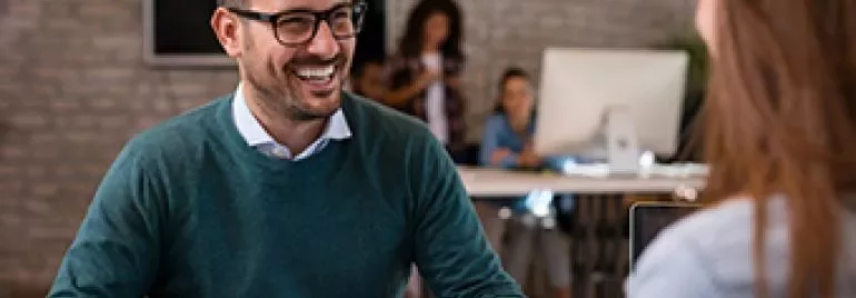 Hombre con gafas sonriendo durante una reunión en oficina moderna.