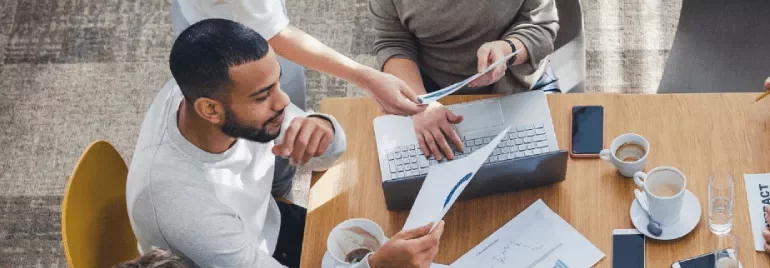Personas trabajando juntas en una mesa con portátiles y documentos.
