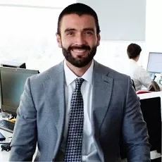 Hombre sonriendo en una oficina con traje gris.