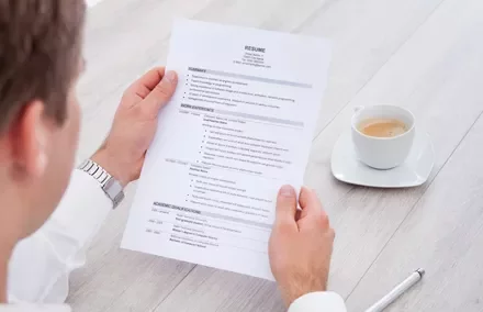 Persona revisando un currículum en una mesa con una taza de café.