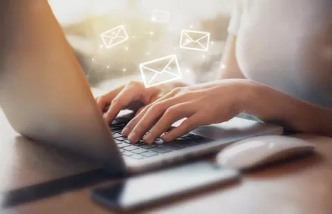 Persona escribiendo en una laptop con iconos de correo alrededor.