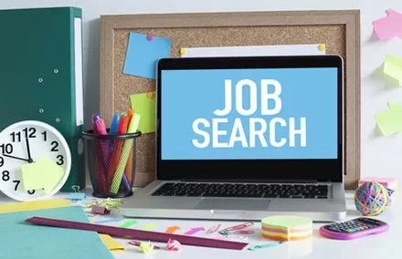 Pantalla de computadora mostrando 'Job Search' entre artículos de oficina.