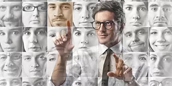 Hombre con gafas interactuando frente a un collage de rostros grises.