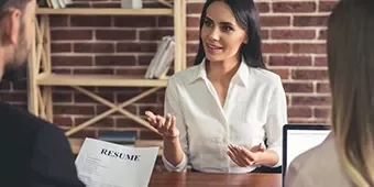 Mujer en entrevista de trabajo, hablando con dos personas que revisan su currículum.