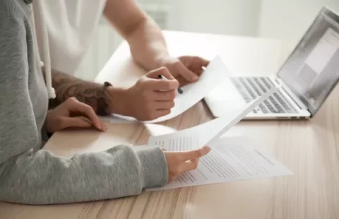 Dos personas revisando documentos en una mesa junto a una laptop.