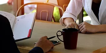 Reunión en una cafetería, manos sobre la mesa y cuaderno abierto.