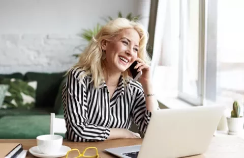 Mujer sonriendo y hablando por teléfono frente a una computadora portátil.