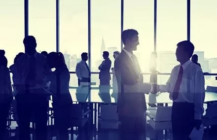 Personas en una reunión de negocios, dos hombres dándose la mano.