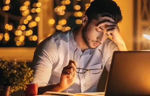 Hombre reflexionando frente a una computadora portátil por la noche.