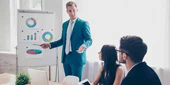 Hombre en traje azul presentando gráficos a colegas en una reunión.