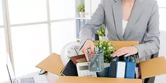 Persona empacando pertenencias de oficina en una caja de cartón.